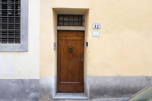 A wooden door with a metal latch, a small window above it, and a number '12' sign on the wall. - CHIESA 12 3P - Florence (Firenze)