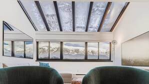 Ein moderner Raum mit Dachfenster, großen Fenstern und Blick auf schneebedeckte Berge.
