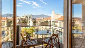 A balcony with two wooden chairs and a small table, overlooking a cityscape with buildings and mountains. - GuestHost - Cozy and modern 70 sqm apartment, able to comfortably accommodate up to 6 people, located on the 5th floor of a modern building with lift (NOT suitable for disabled people). The property is located in an extremely strategic area, just 400 met (Florence)