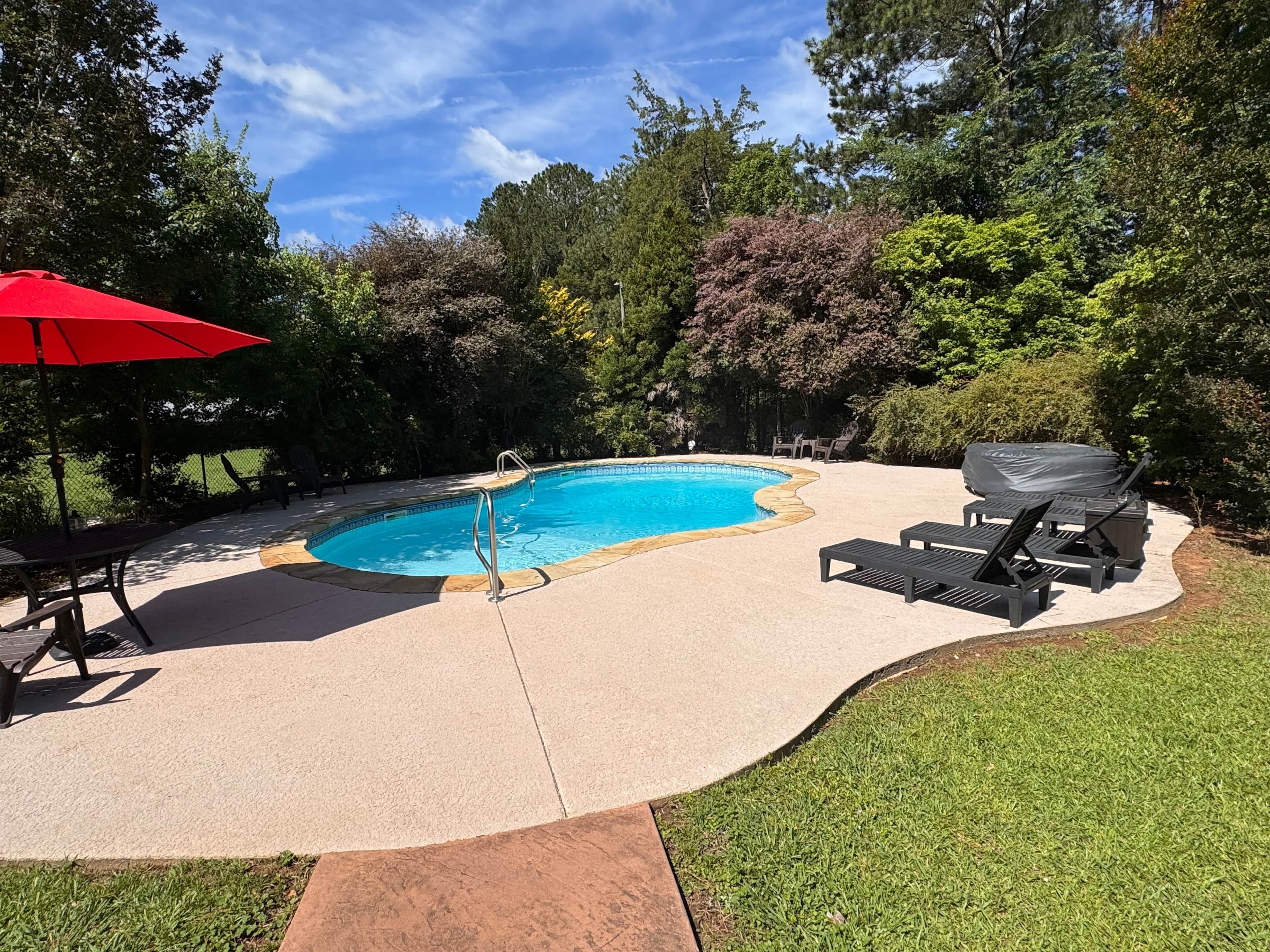 Patio con piscina, un paraguas rojo y mobiliario de exterior.