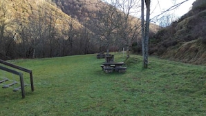 A grassy area with picnic tables and a wooden bench. - My Rooms Hostel Las Salas. Albergue (Las Salas)
