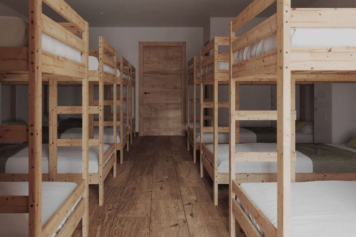 Una habitación con literas dispuestas en dos filas, suelo de madera y una puerta sencilla al fondo.