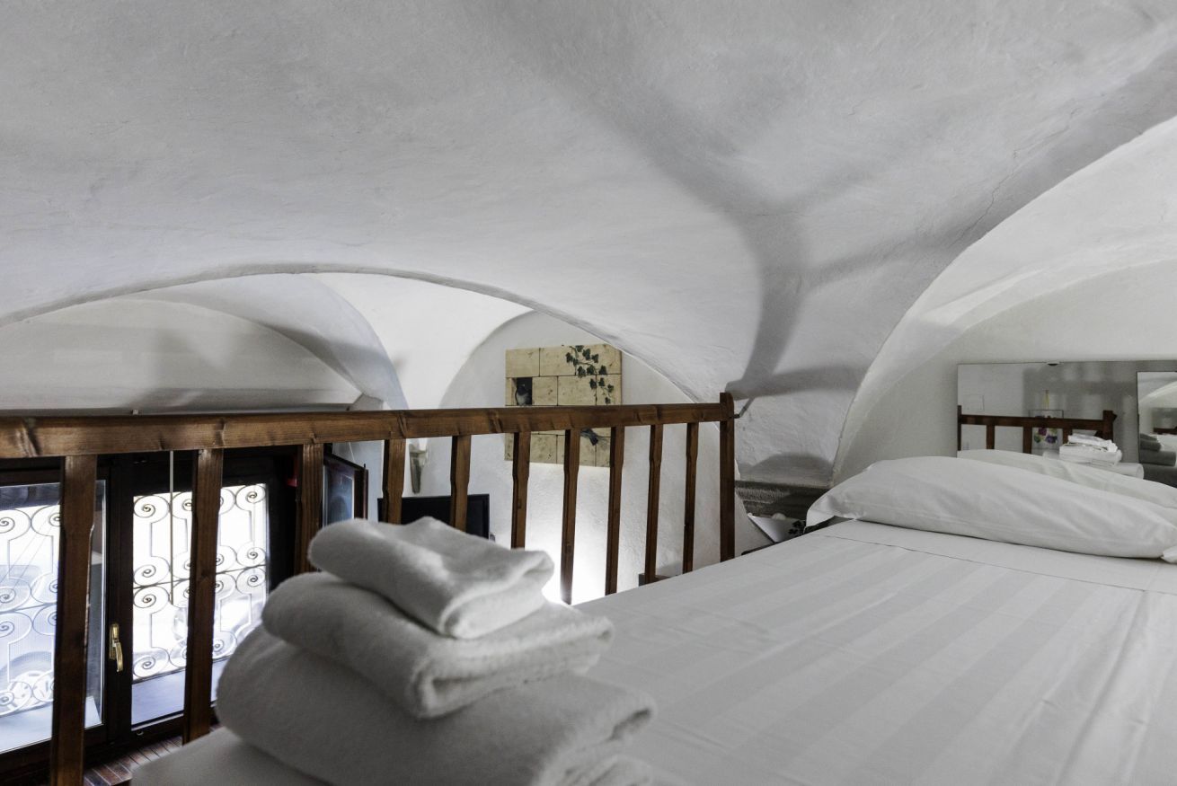 Een slaapkamer met een houten hoofdeinde, een netjes opgemaakt bed en een raam met decoratieve ijzeren tralies.