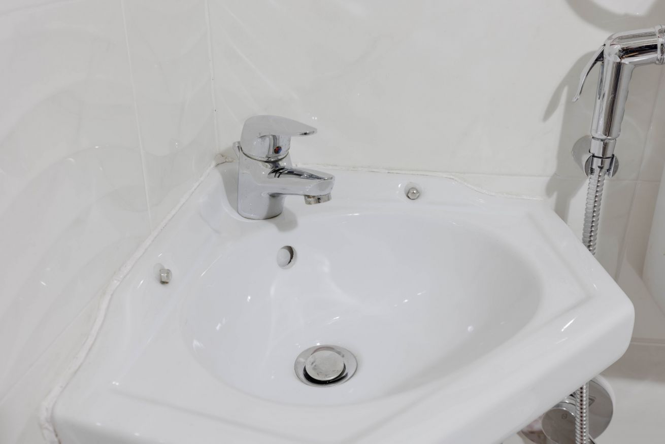 A white bathroom sink with a chrome faucet and a handheld showerhead.