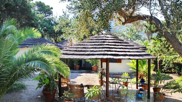 A gazebo with a thatched roof surrounded by potted plants and a small table. - Boutique Villa is an exclusive-use property located along the Tyrrhenian coast, nestled in a pine forest overlooking the sea.The main part of the villa consists of three charming cottages. Inside, you’ll find two bedrooms (one double and one twin), a b (Marina di Caronia)