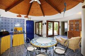 A dining area with a round table and chairs, a kitchen with blue patterned tiles, and a wooden ceiling. - Boutique Villa is an exclusive-use property located along the Tyrrhenian coast, nestled in a pine forest overlooking the sea.The main part of the villa consists of three charming cottages. Inside, you’ll find two bedrooms (one double and one twin), a b (Marina di Caronia)