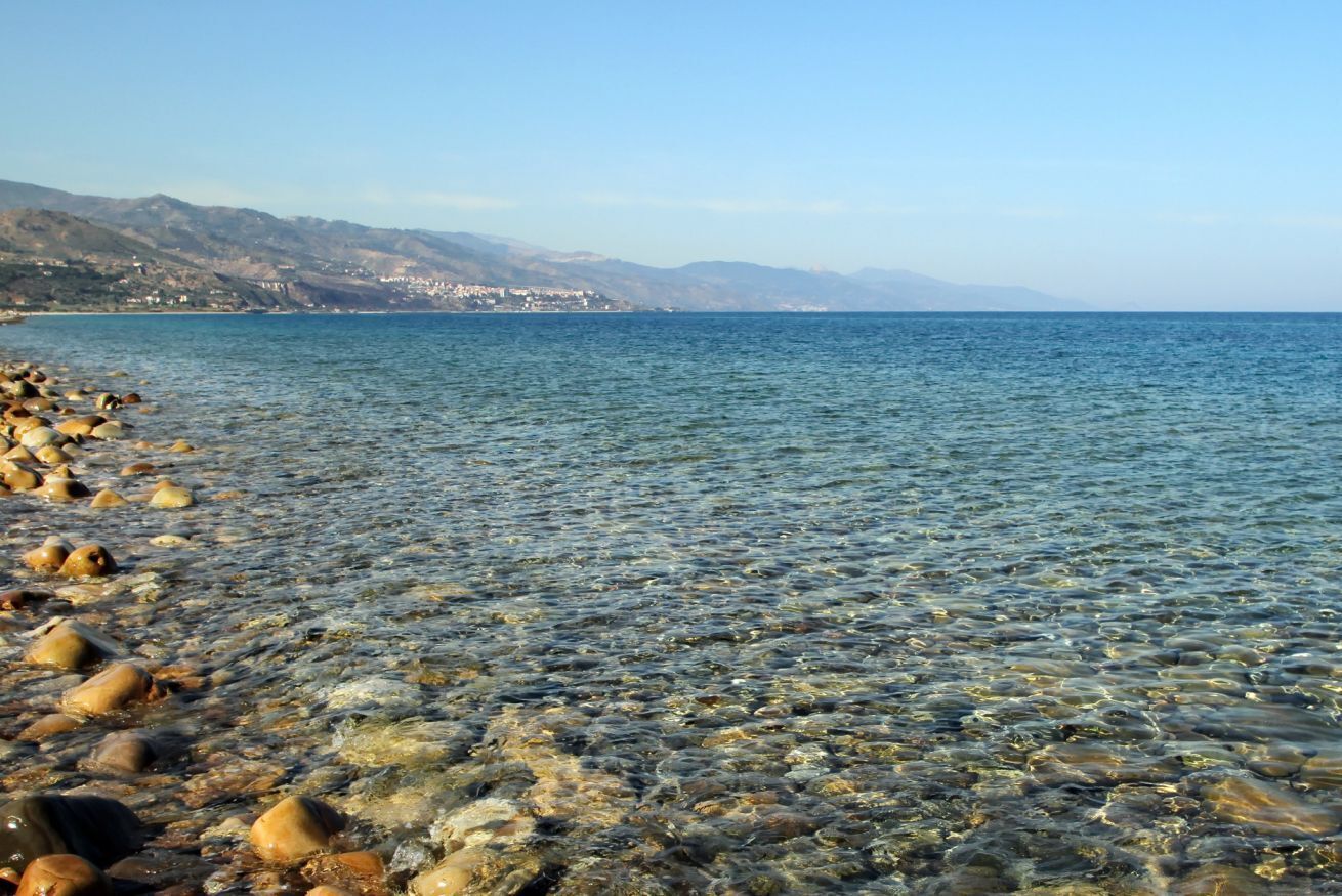 A clear view of a rocky shoreline with a calm sea and distant mountains.