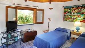 A room with two beds, a TV on a desk, a giraffe decoration, and a colorful quilt on the wall. - Boutique Villa is an exclusive-use property located along the Tyrrhenian coast, nestled in a pine forest overlooking the sea.The main part of the villa consists of three charming cottages. Inside, you’ll find two bedrooms (one double and one twin), a b (Marina di Caronia)