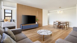 A modern living room with a flat-screen TV, a dining area with a round table and chairs, and a sofa set. - Warm and Cozy Getaway 1BR w/ parking (Honolulu)