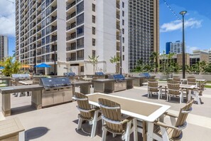 An outdoor patio with barbecue grills and seating, surrounded by tall buildings. - Warm and Cozy Getaway 1BR w/ parking (Honolulu)