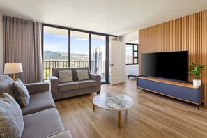 A modern living room with a sofa, a coffee table, and a TV. - Cozy 1BR Condo w/ Lanai, Free Parking & Beach (Honolulu)