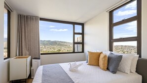 A hotel room with a bed, a radiator, and large windows offering a city view. - Warm and Cozy Getaway 1BR w/ parking (Honolulu)