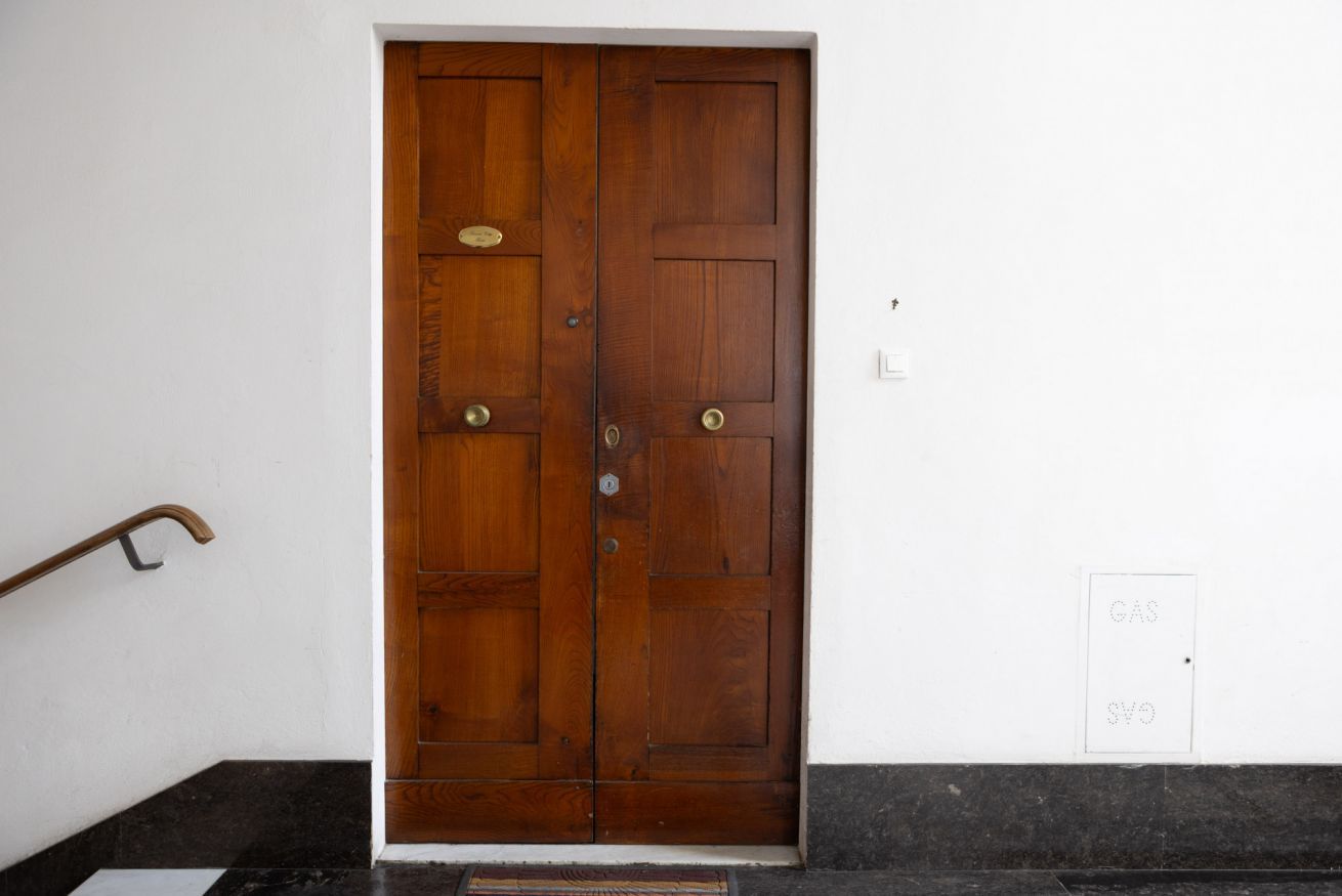 Puerta doble de madera con manija de latón, una placa, felpudo y un enchufe con etiqueta.