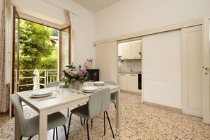 Een eetgedeelte met een tafel voor vier personen, een keuken met witte kasten en een groot raam met uitzicht op groen.
