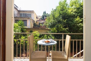 Een balkon met rieten stoelen, een klein rond tafeltje en een croissant.