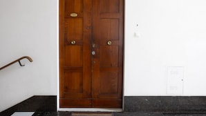 Une porte à double battant en bois, dotée d’une poignée en laiton et d’une plaque, un paillasson et une prise électrique murale avec une étiquette.