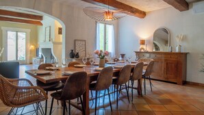 A dining area with a wooden table set for six, surrounded by chairs, a wooden cabinet, and a hanging light fixture. - Casa Limonella - Maison 12 pers avec piscine (Fontvieille)
