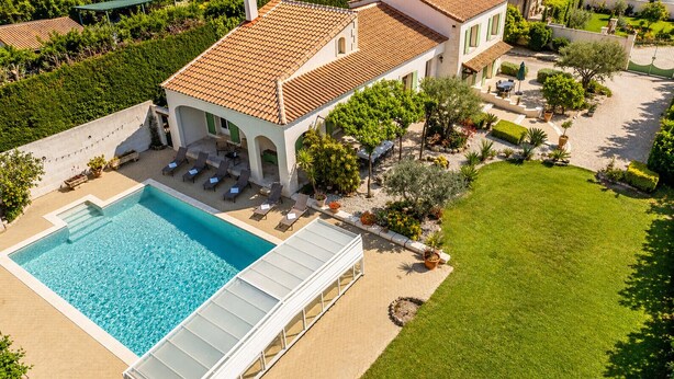 A large swimming pool with a covered deck, a well-maintained lawn, and a building with a tiled roof. - Casa Limonella - Maison 12 pers avec piscine (Fontvieille)
