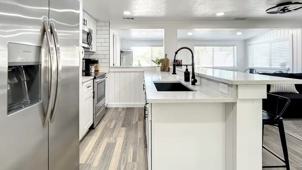 A modern kitchen with white cabinetry, stainless steel appliances, and a central island with a sink. - Charming 3-bedroom vacation home near Siesta Key (Sarasota)