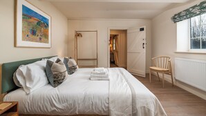 Una cama bien hecha con sábanas blancas y un cabecero verde, una silla de madera y un cuadro enmarcado en la pared.