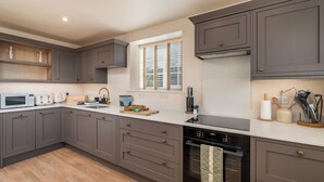 Una cocina moderna con armarios grises, horno empotrado y ventana con persianas.