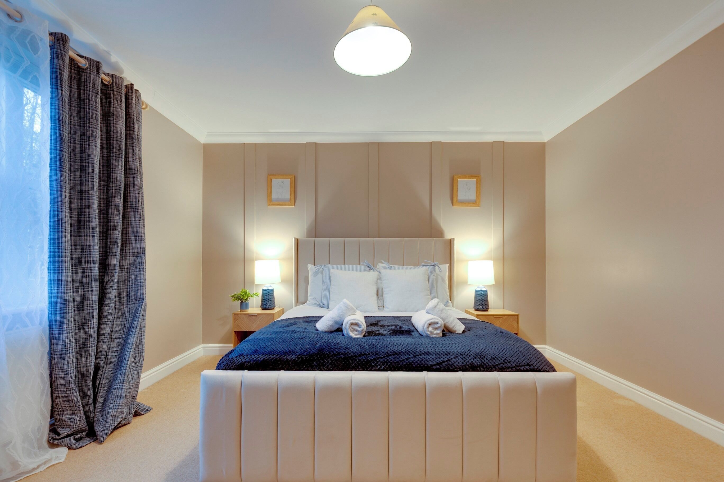 A neatly made bed with a blue blanket and white pillows, two bedside lamps, and a small plant on a nightstand.