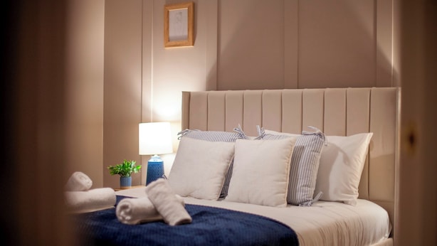 Een net opgemaakt bed met een gestreept kussen, een blauwe sprei en een kleine potplant op het nachtkastje.
