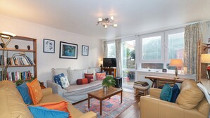A well-lit living room with a sofa, armchairs, a coffee table, and a bookshelf. There is a television and a window with curtains. - Homely flat by the river in Battersea, SW London - Pass the Keys (London)