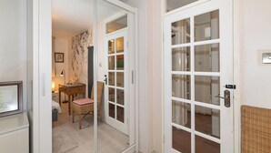 A room with a sliding glass door leading to a balcony, a wicker chair, a small table with a lamp, and a framed picture on the wall. - Homely flat by the river in Battersea, SW London - Pass the Keys (London)