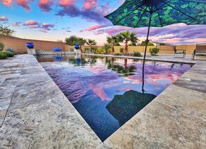 Una piscina con reflejo cristalino, rodeada de palmeras y un cielo al atardecer.