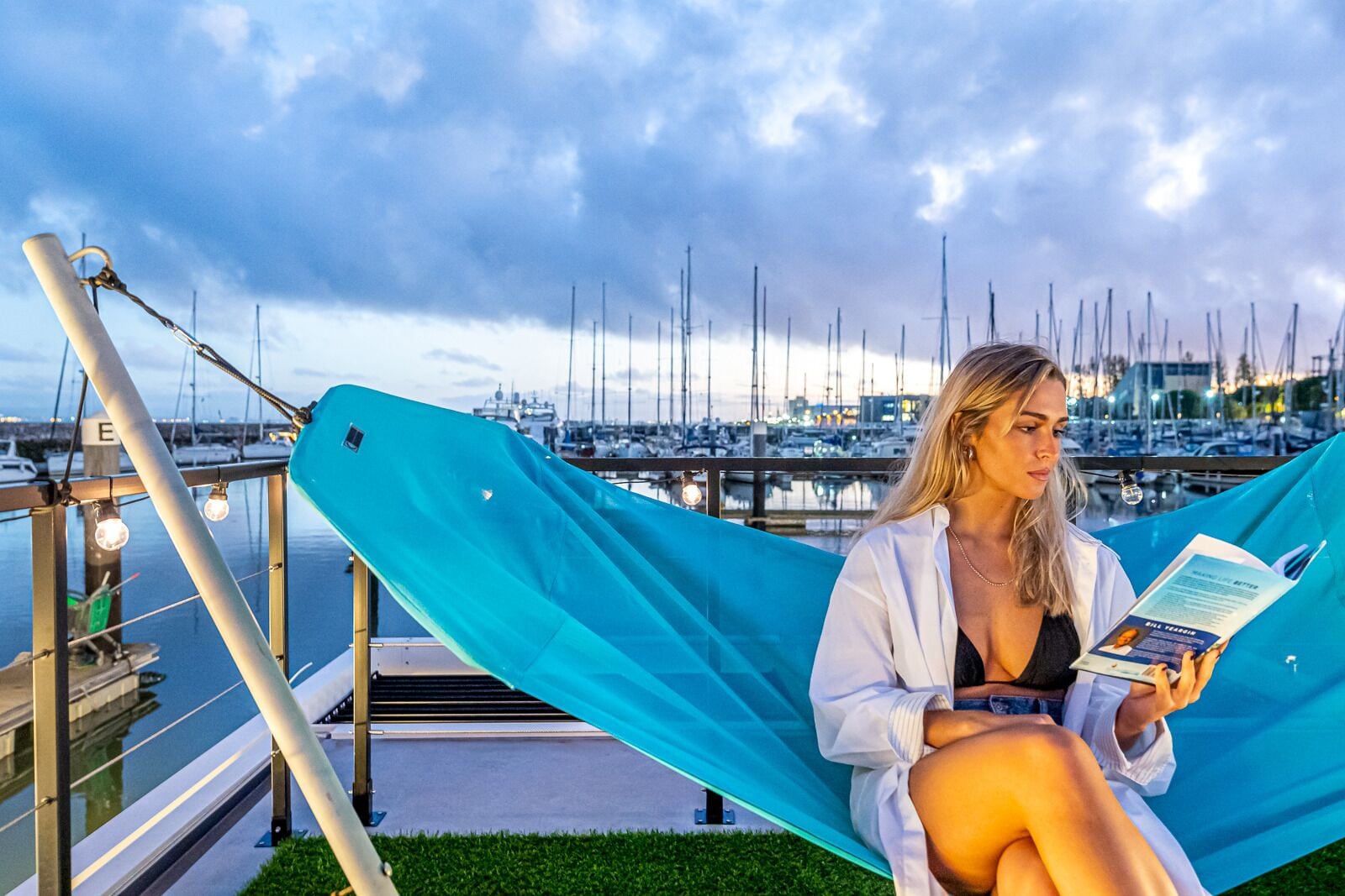 A person sitting on a hammock by a marina with boats in the background.