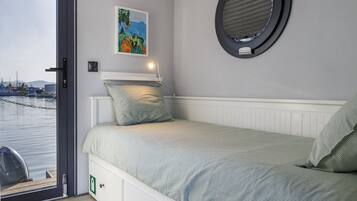 A bedroom with a bed, a window, a door, and a view of the water outside.