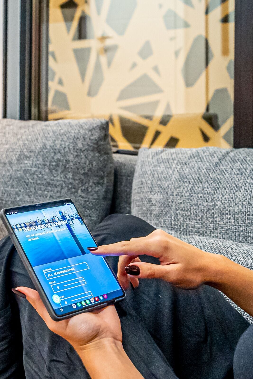 A person using a smartphone on a couch with a patterned wall in the background.