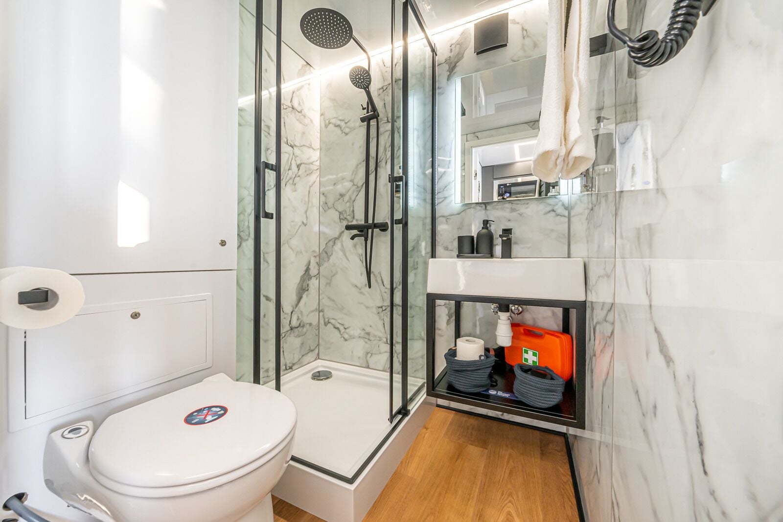 A bathroom with a glass-enclosed shower, a toilet, and a sink with toiletries.
