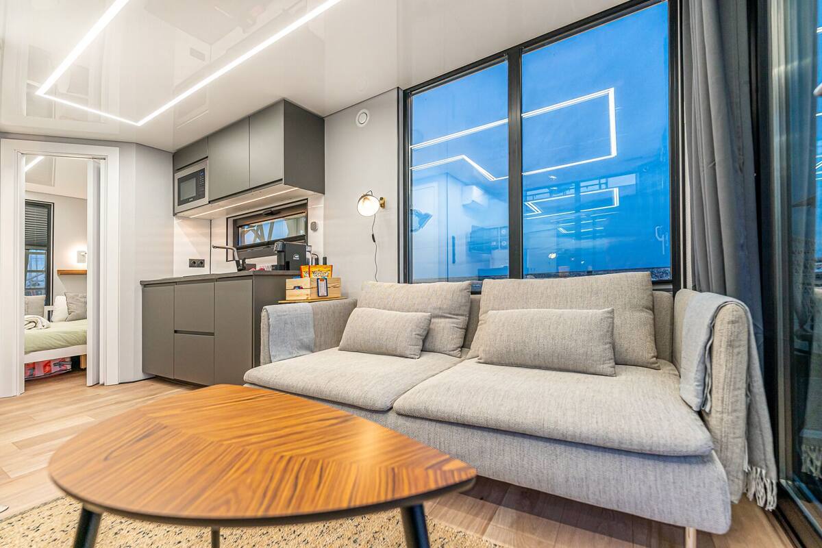 A modern living room with a sofa, a wooden coffee table, and a kitchen area with a microwave.