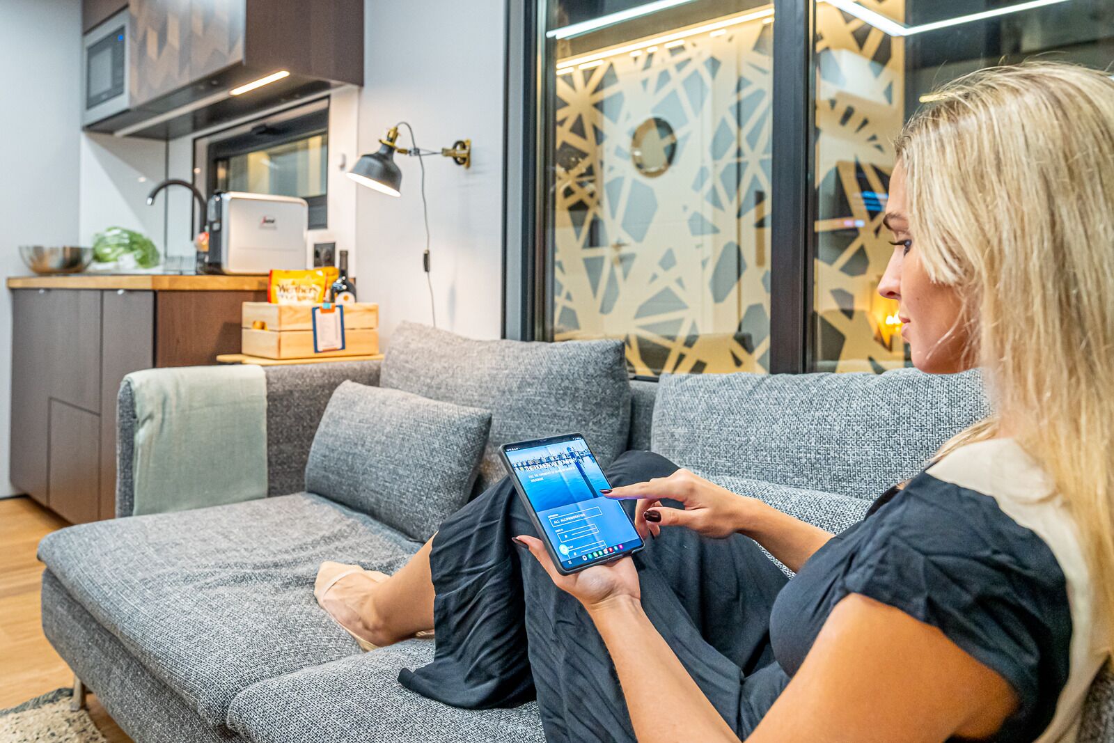 Un soggiorno moderno con un divano grigio, un portatile sul tavolino e una parete decorativa con motivi geometrici.