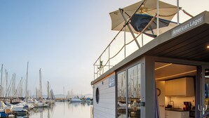 A glass-walled boat with a covered deck and a kitchen area, docked at a marina with other boats. - The Homeboat Company Sant'Elmo-Cagliari (Cagliari)