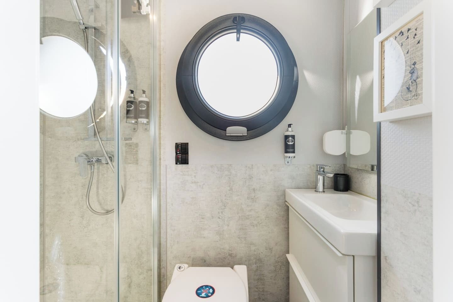 Een moderne badkamer met een glazen douchecabine, een ronde spiegel, een toilet en een wastafel met zeepdispenser.