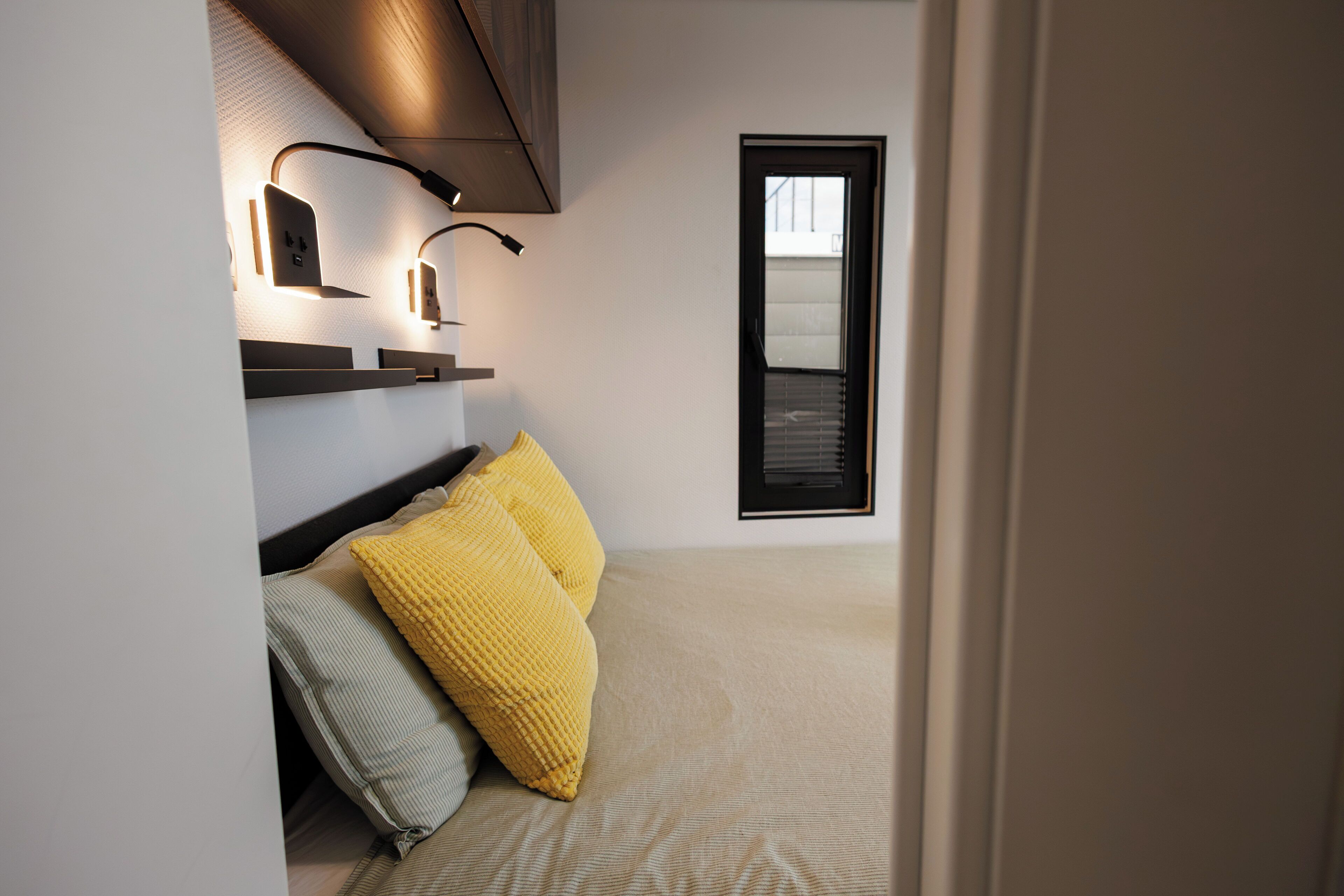 Um quarto moderno com cama, duas almofadas, mesa de cabeceira e iluminação embutida na parede.