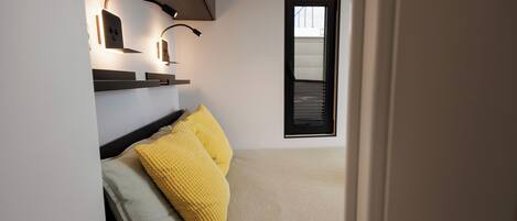 Um quarto moderno com cama, duas almofadas, mesa de cabeceira e iluminação embutida na parede.
