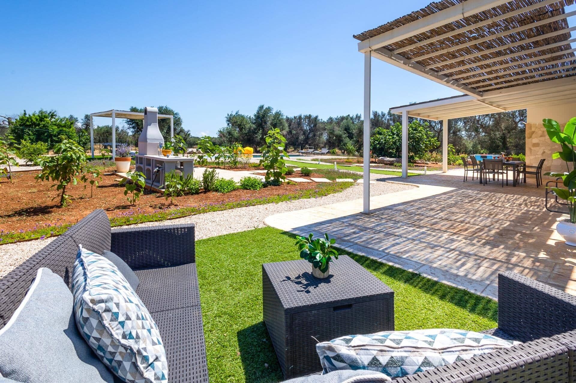 Ein Terrassenbereich im Freien mit Korbmöbeln, einem Grill und einer überdachten Sitzgelegenheit.