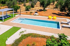 A rectangular swimming pool with a wooden deck, surrounded by a gravel area and a grassy patch. - Villa Mastroronzo by Villa Plus (San Vito dei Normanni)