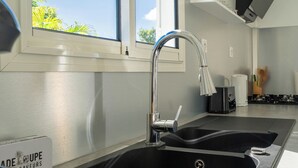 Een moderne keuken met een roestvrijstalen spoelbak, een raam met uitzicht op groen en een bordje dat een 'Made in France' product aanduidt.