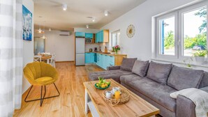 A modern living room with a grey sofa, a wooden coffee table with breakfast items, and a yellow chair. A kitchen with blue cabinets is visible in the background. - Villa Azurno by Villa Plus (Juršići)