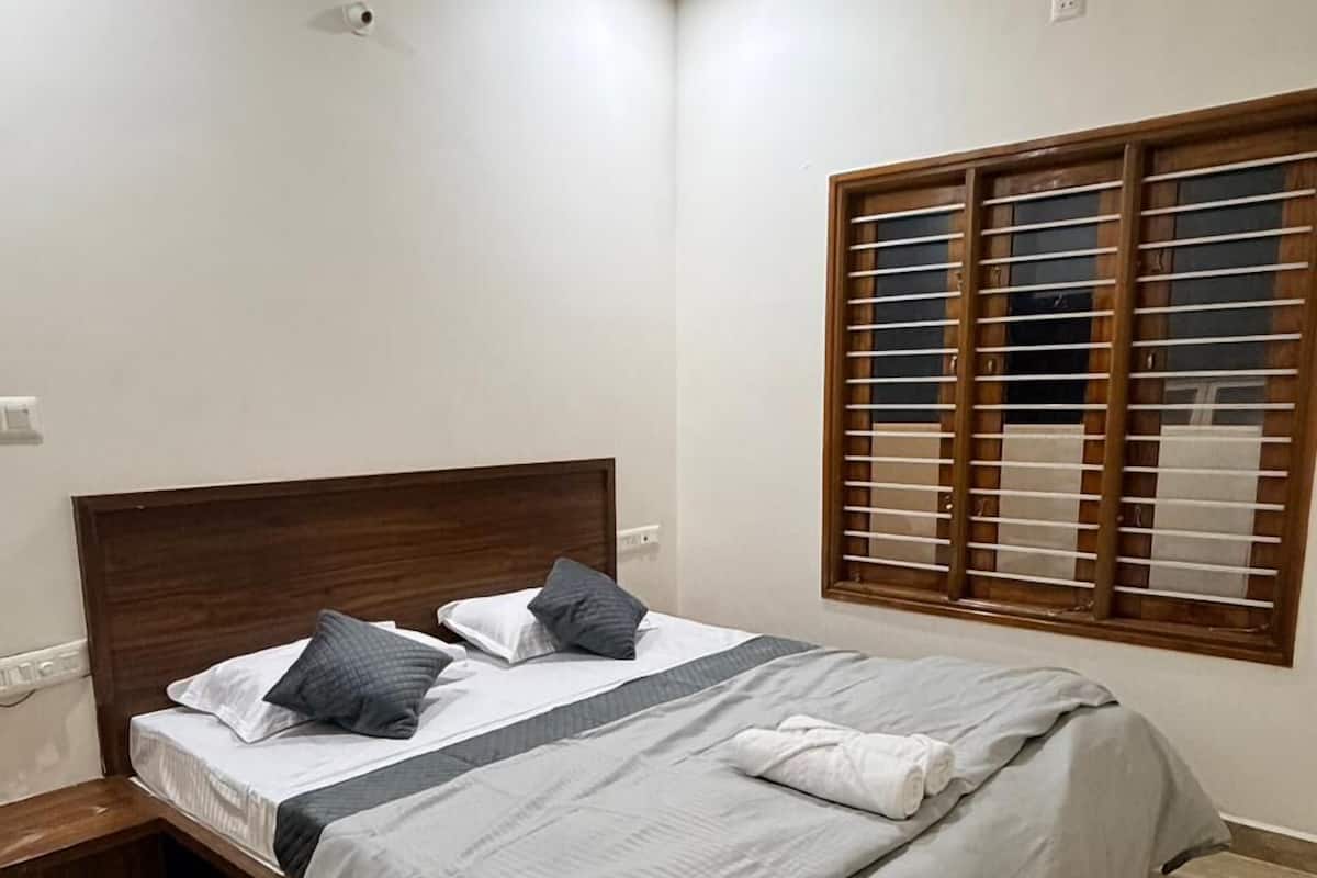 Una cama doble bien hecha, con cabecera de madera, mesita de noche y ventana con persianas de madera.