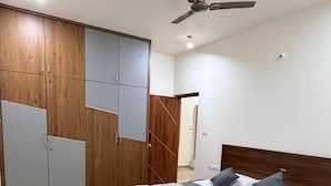 A bedroom with a bed, a ceiling fan, a wardrobe, and a small rug. - The Residence 267 Homestay (Mysore)