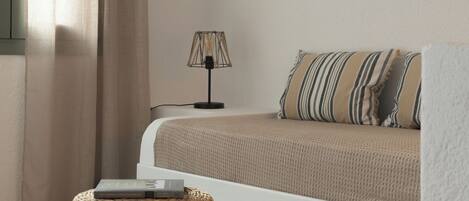 A bedroom with a bed, a bedside lamp, a woven ottoman, and wall art.