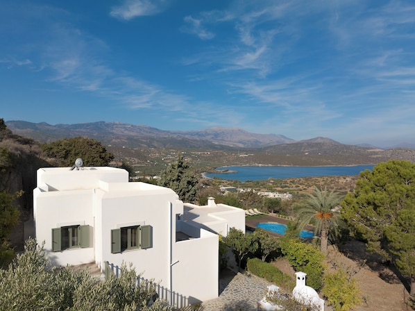 A white building with a pool and a view of mountains and a lake.