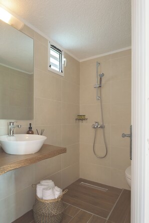 A bathroom with a white sink, a mirror, a shower, and a small window.