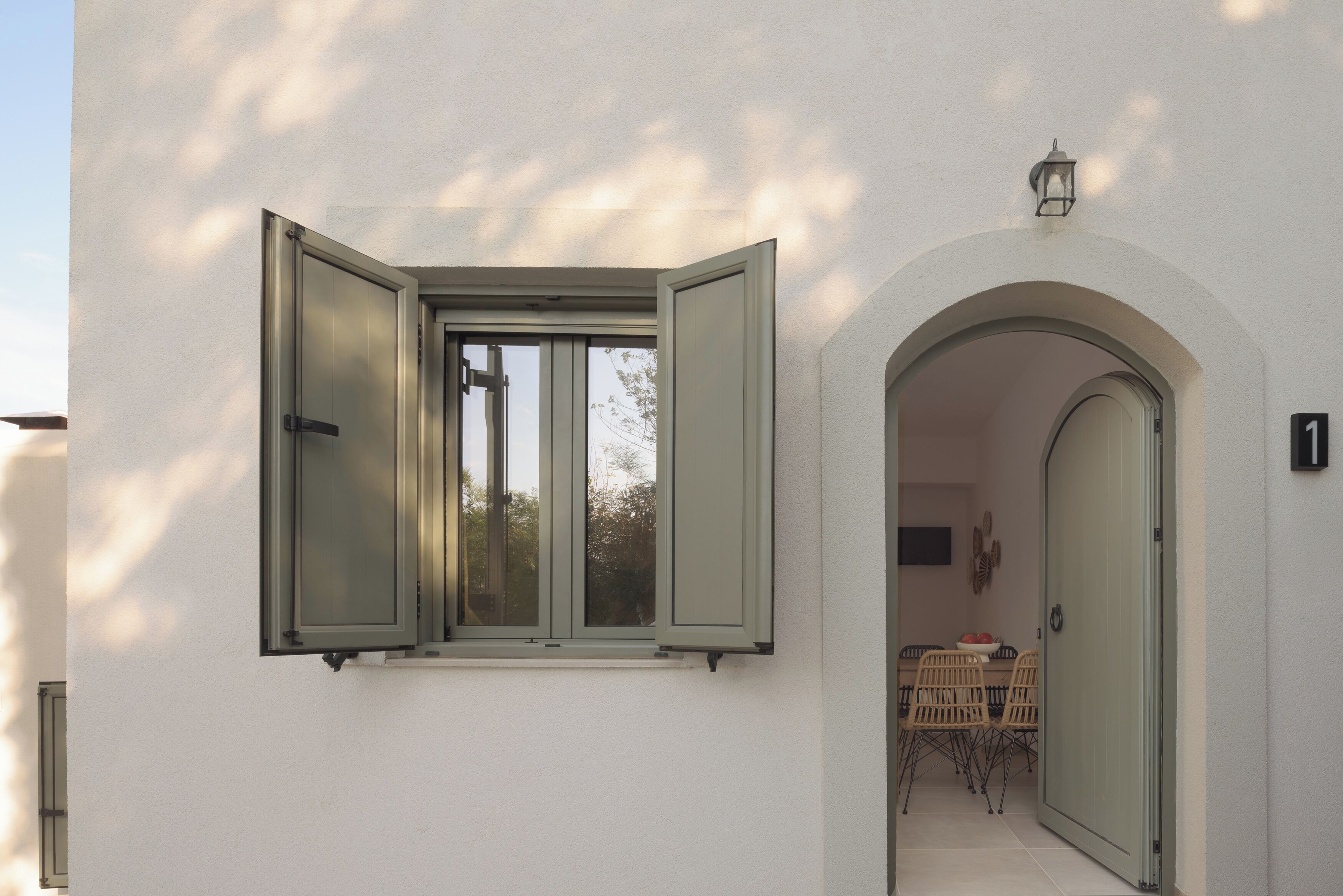 Un edificio blanco con un gran ventanal y una puerta abierta que da a un comedor con mesa y sillas.